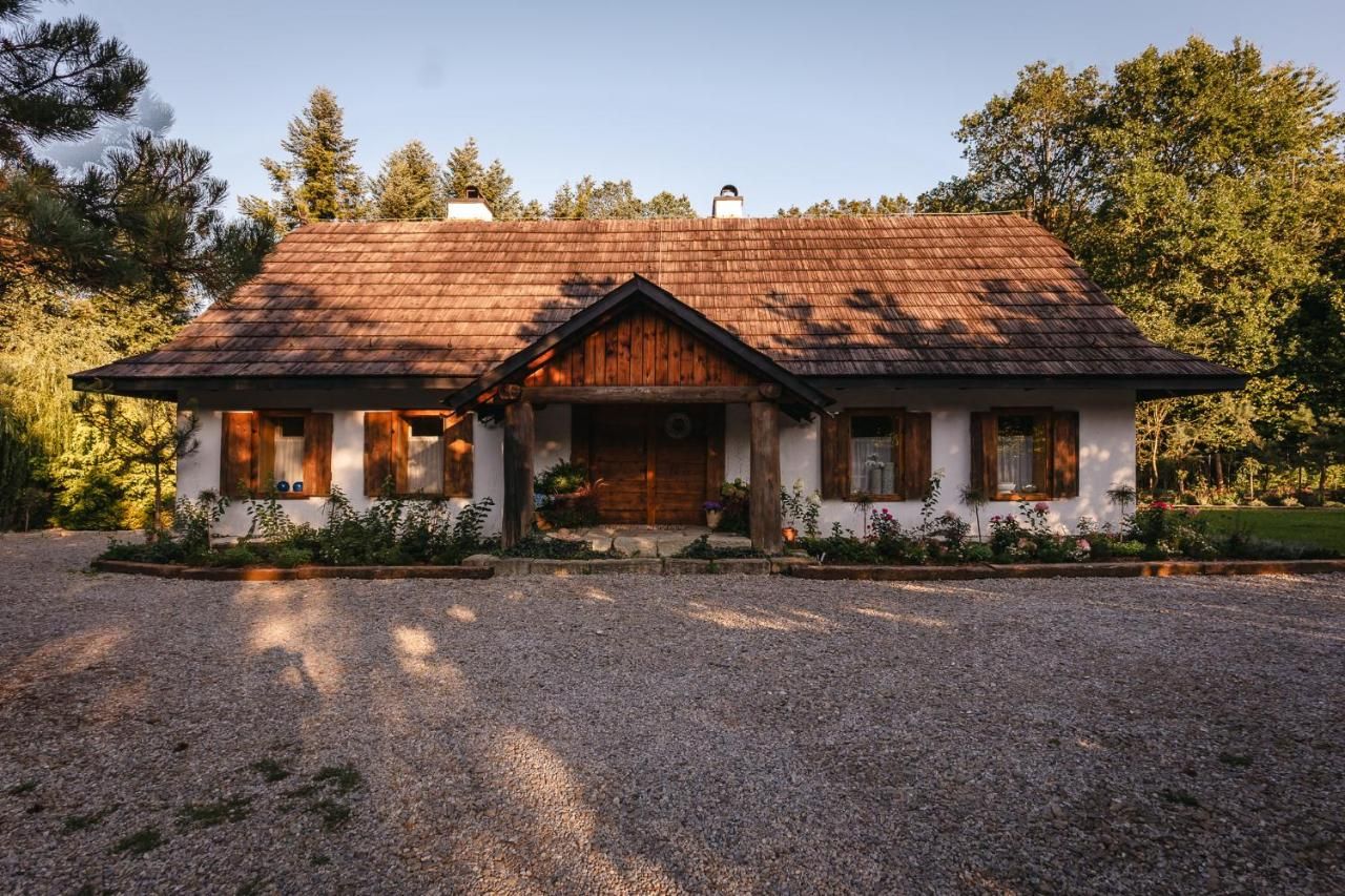 Chata od frontu, przed nią żwirowy podjazd i kwiaty pod oknami