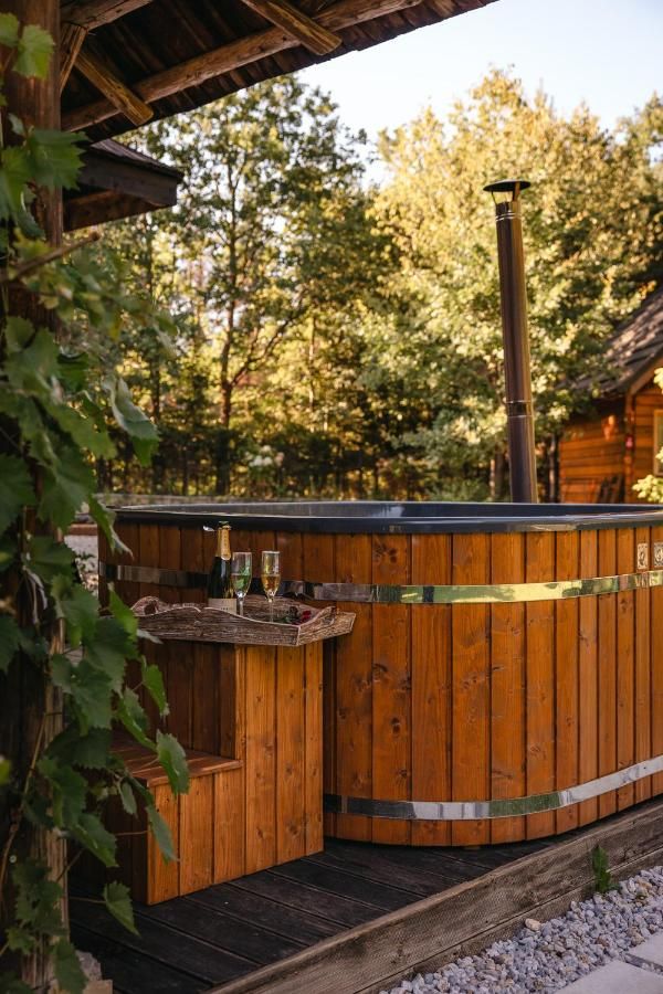 Drewniana wanna z hydromasażem pod zadaszeniem, na brzegu dwa kieliszki